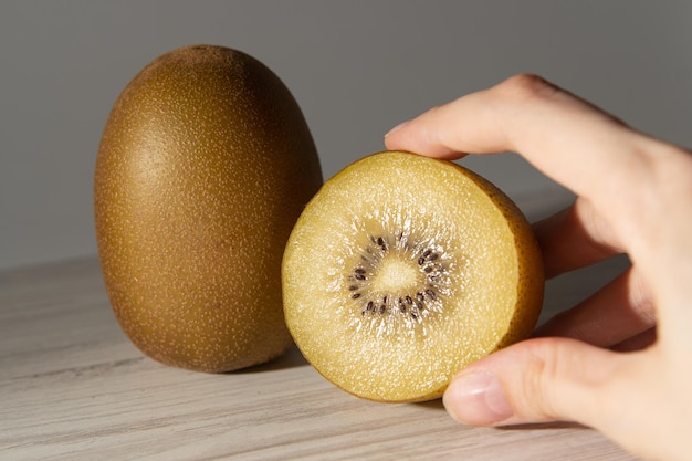 Deux kiwis jaunes coupés sur une table grise avec des ombres dans leurs mains Gros plan