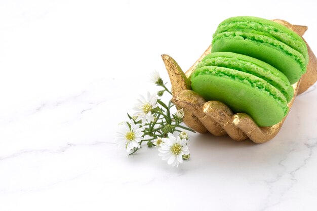 Deux macarons verts sur une main en bois dorée avec de minuscules fleurs blanches. Fond haut en marbre.