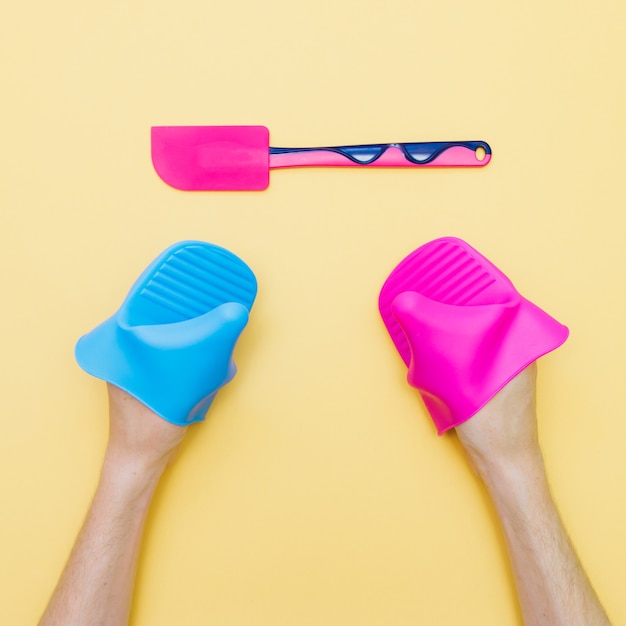 deux mains dans des gants en silicone rose et bleu essayant de prendre une truelle de cuisine