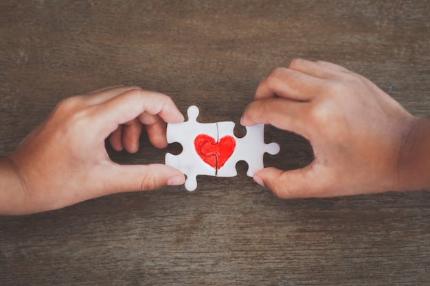 Deux mains d'enfant reliant pièce de puzzle couple avec coeur rouge dessiné