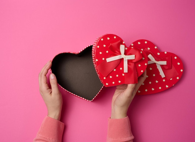 Deux mains féminines tiennent une boîte en forme de coeur rouge sur fond rose