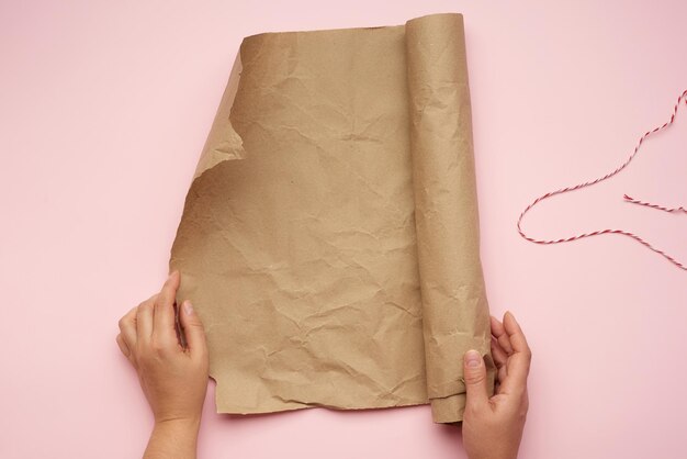 Photo deux mains féminines tiennent un rouleau de papier brun sur un fond rose.