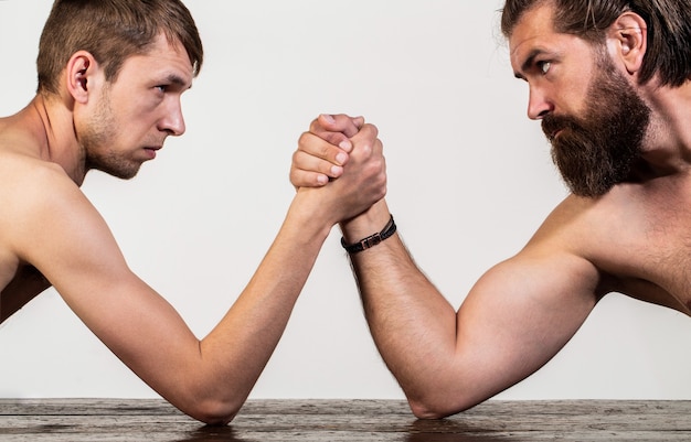 Deux mains d'homme jointes bras de fer, match fort et faible, inégal. Homme barbu fortement musclé luttant contre un homme faible et chétif. Bras de lutte main mince, grand bras fort