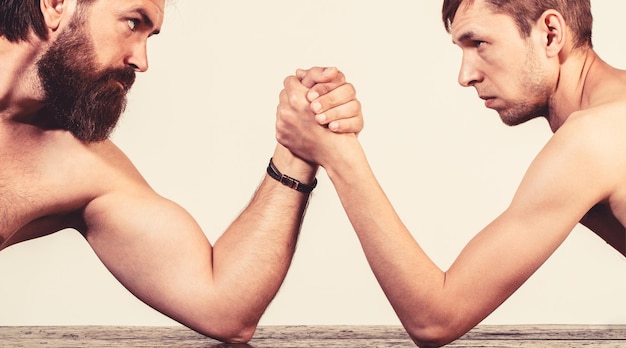 Photo deux mains d'homme jointes bras de fer match inégal fort et faible homme barbu fortement musclé bras de fer un homme faible chétif bras de fer main mince gros bras fort en studio