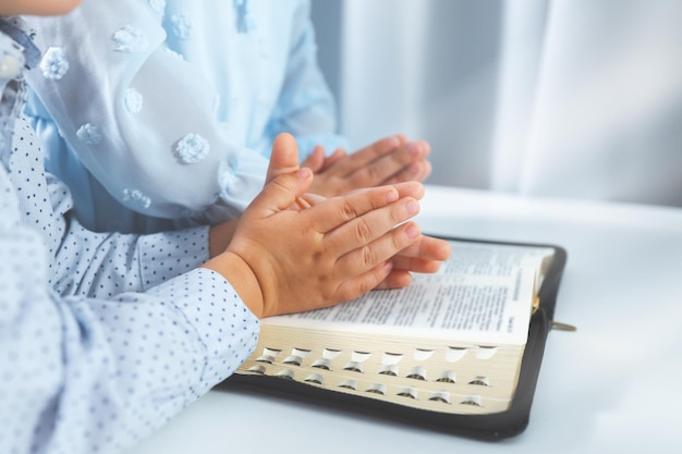 Deux mains de petite fille et de garçon jointes en prière sur une Sainte Bible ensemble pour le concept de foi