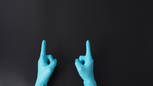 Deux mains portent des gants bleus de médecin et pointent le doigt sur un fond noir