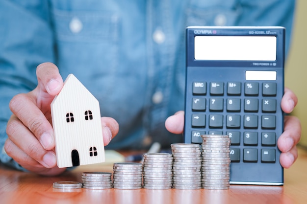 Photo les deux mains tenaient une maison et une calculatrice, et des pièces de monnaie empilées devant