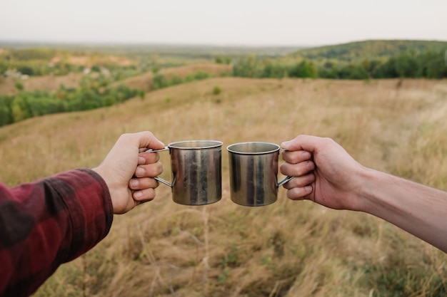 Deux mains tenant des bouchons touristiques en métal dans la belle nature. Les hommes saluant des boissons au sommet de la colline lors d'une randonnée