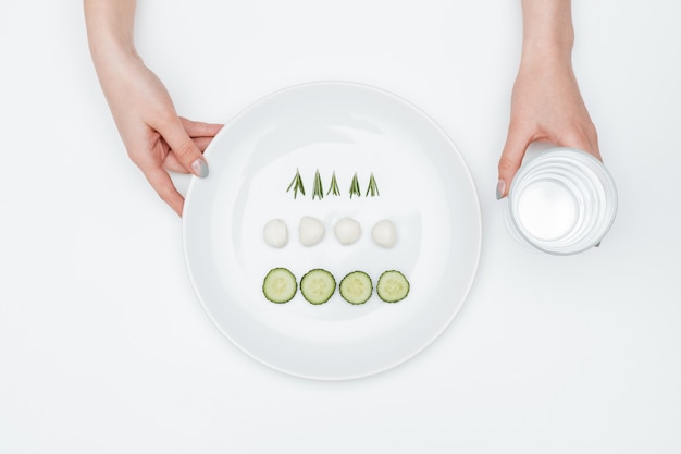 Deux mains tenant un verre d'eau et une assiette avec du concombre, de la mozzarella et des herbes