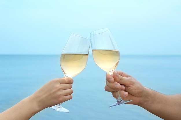 Deux mains tenant des verres à vin sur fond de mer