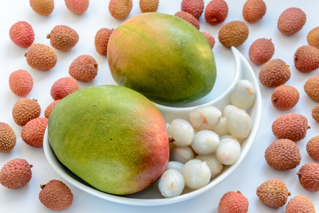 Deux mangues mûres entourées de fruits de litchi mûrs sur une assiette sur fond blanc. Litchi mûr sans coquille.