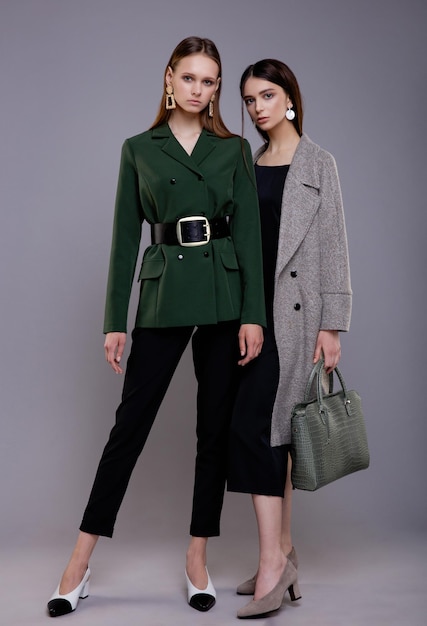 Deux mannequins en costume vert pantalon noir ceinture large et manteau gris avec sac