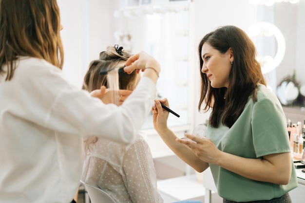 Deux maquilleurs appliquent les cheveux et le maquillage à la mariée dans le dressing