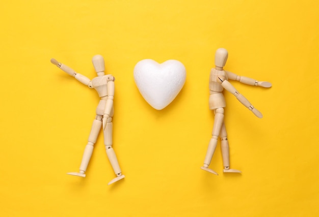 Photo deux marionnettes et un cœur sur un fond jaune concept d'amour vue du haut