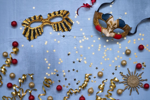 Photo deux masques de carnaval, étoiles de confettis et banderoles de fête sur fond bleu.