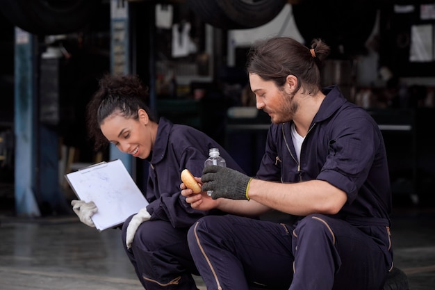 Deux mécaniciens automobiles masculins et féminins se détendent et grignotent pendant leur pause déjeuner.