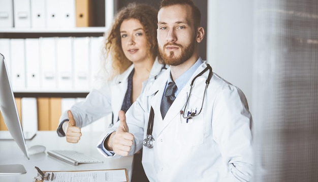 Deux médecins assis avec les pouces vers le haut au bureau de l'hôpital. Aide médicale, lutte contre l'infection virale et concept de médecine.