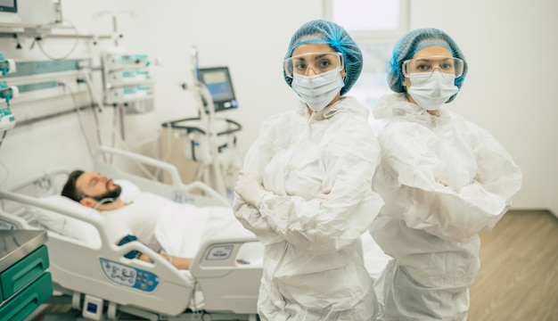 Deux médecins confiants en combinaisons de protection debout sur le fond d'un patient atteint de coronavirus