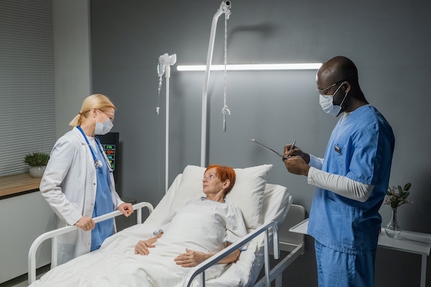 Deux médecins debout près du lit avec une femme âgée et se renseignent sur sa santé dans la salle d'hôpital