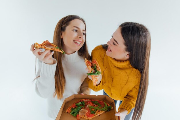 Deux meilleurs amis mangeant une pizza appétissante. Filles souriantes, regardant la caméra et posant.