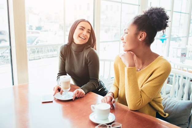 Deux meilleurs amis sont assis dans un café et passent du bon temps ensemble. Les filles boivent du café au lait et apprécient leur conversation.