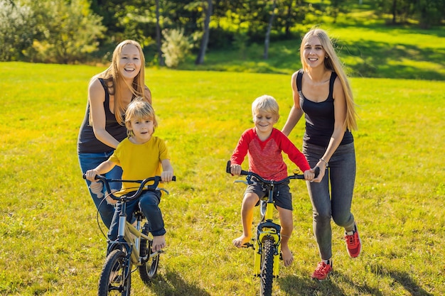 Deux mères heureuses apprennent à leurs fils heureux à faire du vélo.