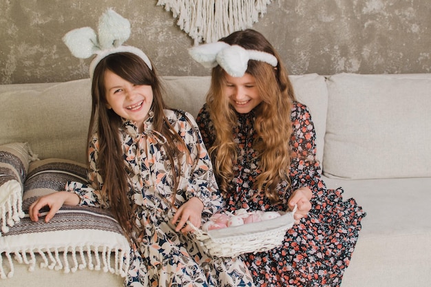 Deux mignonnes petites filles aux oreilles de lapin sont assises sur le canapé avec des paniers de Pâques