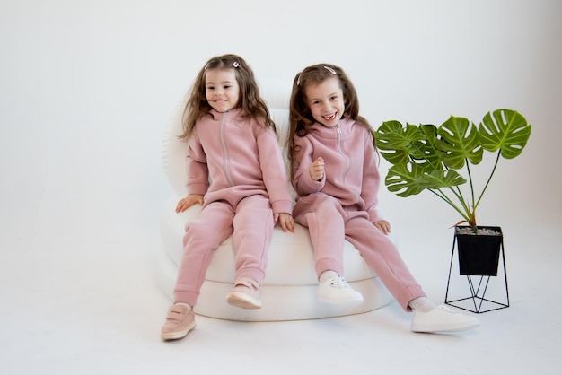 Deux mignonnes petites filles dans une salopette rose sont assises sur une chaise blanche Fond blanc Mode Enfance