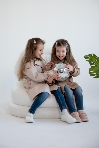 Deux mignonnes petites filles dans des trench-coats identiques sont assises sur une chaise blanche