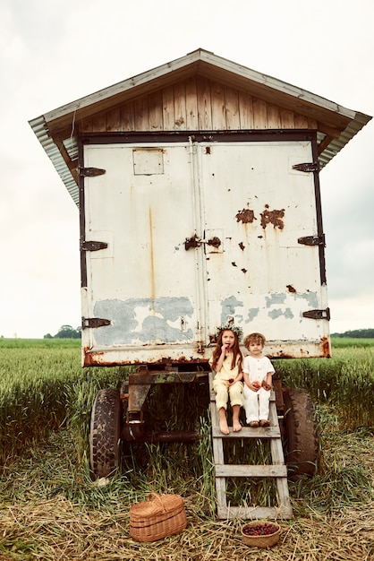 Deux mignons enfants garçon et fille vêtus de tissu de lin blanc récolte des fraises dans le domaine et s'amuser près de la remorque