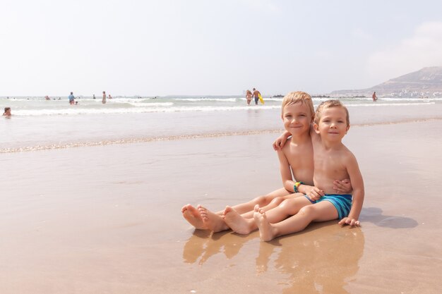 Deux mignons petits garçons adorables frères assis sur la plage océan mer