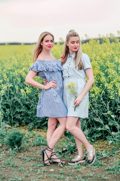 Deux modèles de filles posant ensemble devant la caméra dans le champ de colza