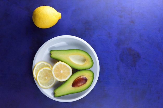 Deux moitiés d'un avocat mûr avec des graines sur une plaque blanche Libre de fruits verts sains avec des agrumes sur un fond bleu