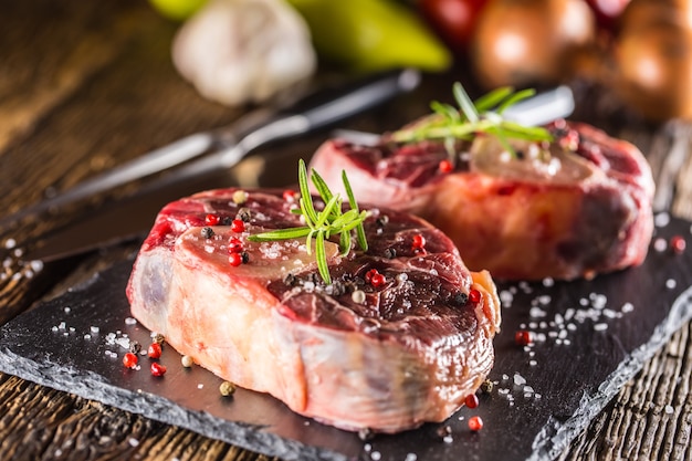 Deux morceaux de jarret de boeuf cru sur ardoise et table en bois.