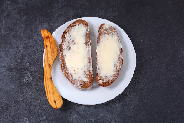 Deux morceaux de pain artisanal avec du beurre et un couteau en bois sur une plaque blanche