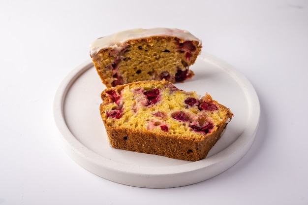 Deux morceaux de petit gâteau fait maison avec des canneberges et du sucre glace sur une plaque blanche sur une lumière