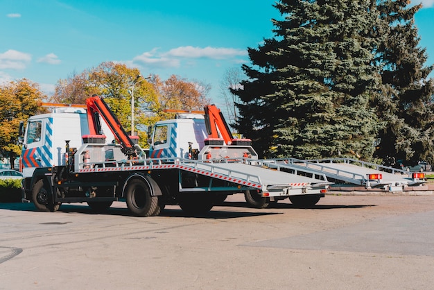 Deux nouvelles dépanneuses stationnées près de la route de la ville. Grues sur camion pour remorquer des voitures. Urbain. Un service. Vue de côté. Remorques avec élévateurs