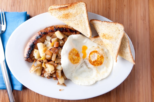 Deux œufs sur facile, saucisse, pommes de terre rissolées et pain grillé