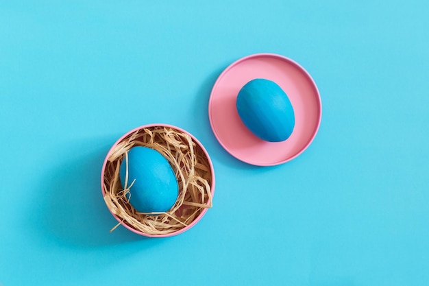 Deux oeufs de Pâques bleus se trouvent dans des boîtes en métal rose vif Fond bleu Espace de copie