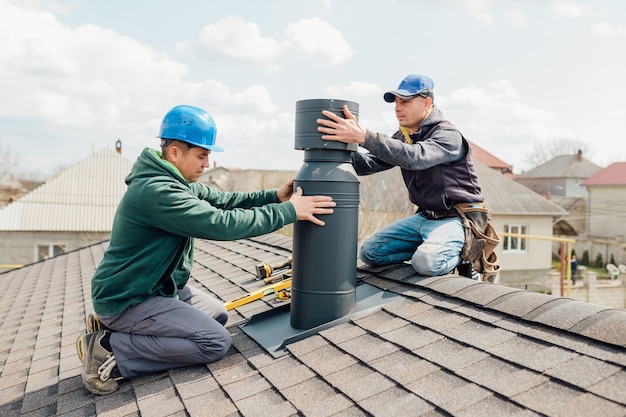 Deux ouvriers professionnels debout sur le toit et mesurant la cheminée de la nouvelle maison en construction sur fond bleu