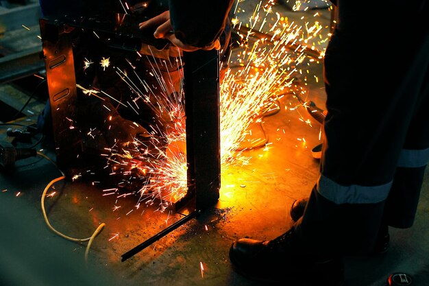 Deux ouvriers soudent une pièce métallique dans un atelier sur le lieu de travail Étincelles de soudure lumineuses