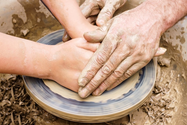 Deux paires de mains - homme et femme, ou jeune et vieux - créent un produit en argile sur un tour de potier