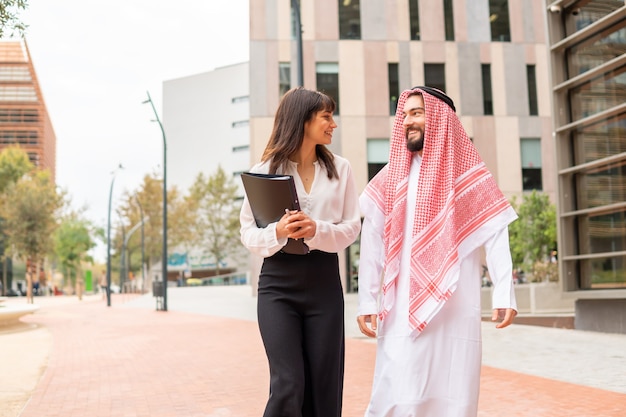 Deux partenaires commerciaux multiraciaux homme arabe et femme européenne parlant agréablement à l'extérieur