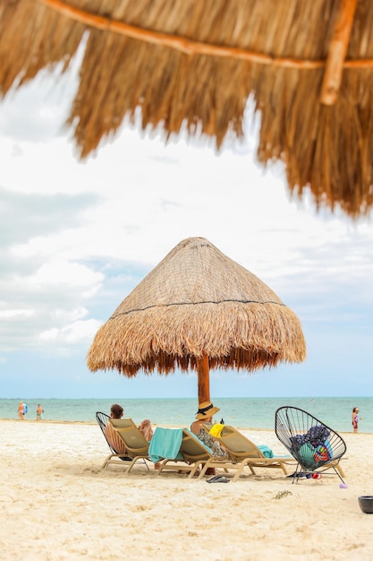 Deux personnes assises sur une plage avec un parasol en chaume