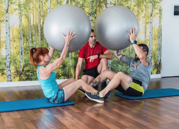 Deux personnes faisant des abdominaux avec un ballon de Pilates avec leur entraîneur personnel dans une salle de sport