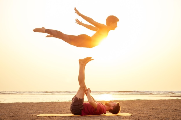 Photo deux personnes pratiquant le yoga à la lumière du coucher du soleil sur la plage de goa en inde. femelle et mâle acro yogi tantra volant copyspce.