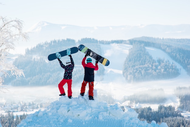 Deux personnes se tiennent dos à la neige et lèvent leurs planches à neige
