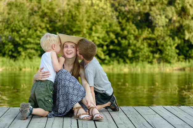 Deux petit fils s'embrasser et étreindre sa mère assise sur un ponton au bord de la rivière