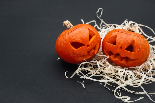 Deux petites citrouilles sculptées, sur fond noir.