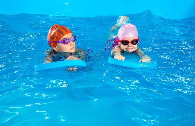 Deux petites filles apprennent à nager dans une piscine à l'aide de planches à flotter